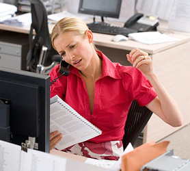 Stressed-out woman talks on phone at office desk